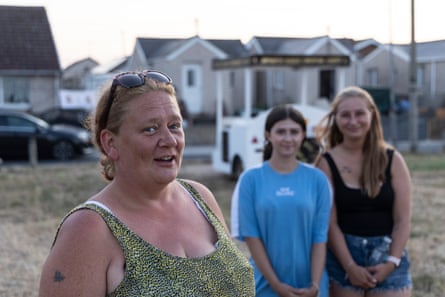 A woman in her 40s stands in the front of the frame, slightly to the left, with two younger women out of focus behind her