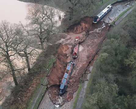 An aerial view of a narrowboat perched on the edge of a sinkhole, with two others in it