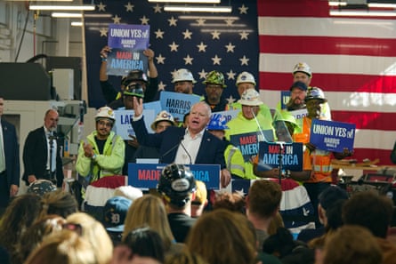 a walz in front of a crowd as construction workers stand behind him