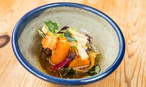 A biscuit-coloured bowl with a blue rim. Inside, chunks of carrot and other vegetables in a dark soup