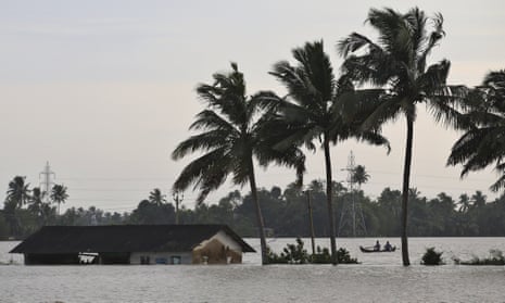 Two men row a boat through a flooded paddy field next to an inundated structure in Alappuzha in the southern state of Kerala, India.