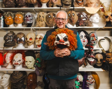 Park director Ben Francis holds up a clown mask as he stands in front of shelves filled with different scary masks.