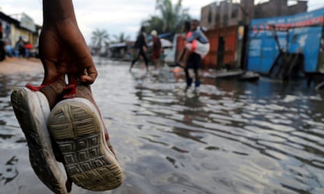 A Congolese man carries his shoes as he wades through floodwaters