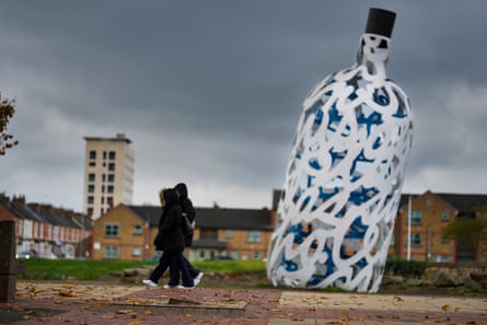 Two people walk past a large bottle-shaped sculpture in Middlesbrough’s civic square under a cloudy sky