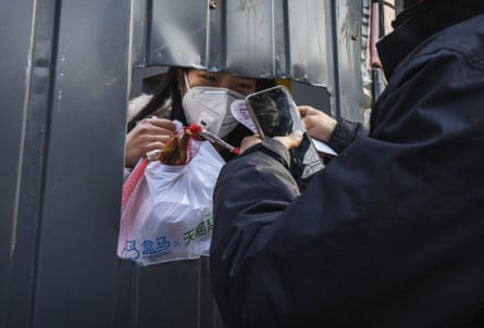 A woman wears a protective mask as she accepts a package from a courier through a hole in a makeshift barricade wall
