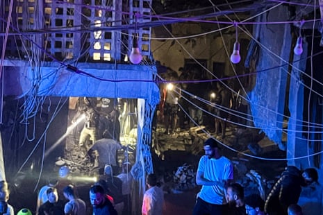 People crowd around a destroyed building in the evening.