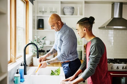 Medium wide shot of smiling father and son washing fresh vegetables in kitchen sink