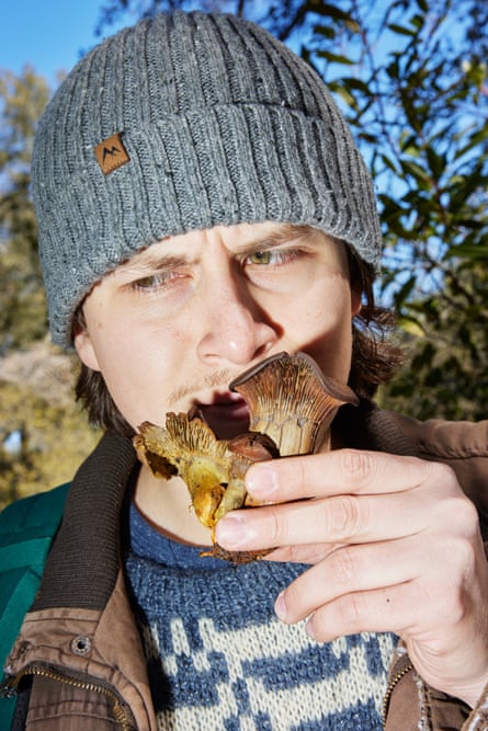 A man in a beanie smells a mushroom