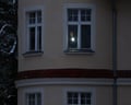 View from outside the building of a man standing at a window shining his torch from inside a dark room