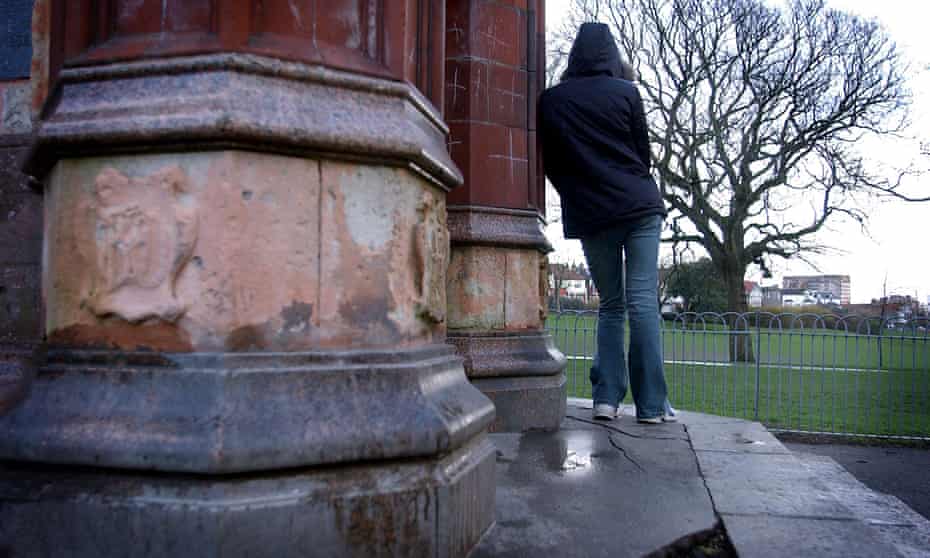 A teenager stands in a park with her back to camera