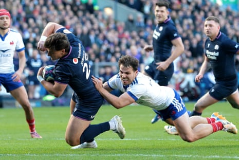 Tom Jordan of Scotland scores his team's seventh try whilst under pressure from Antoine Dupont of France.