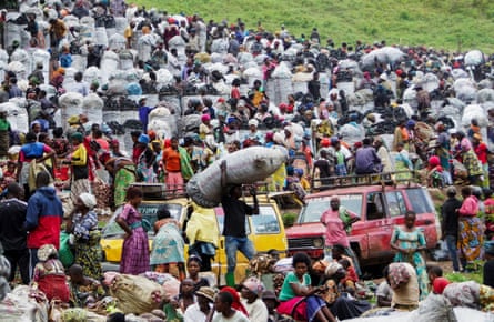 A huge crowd of people on a grassy slope, some carrying or standing with large grey sacks of charcoal.