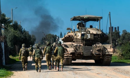 IDF soldiers walk on foot alongside a military tank