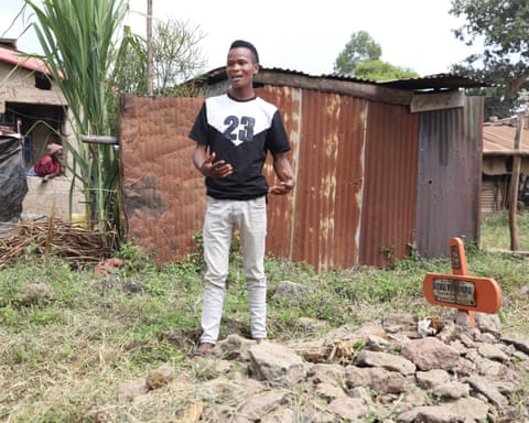 Brian Kuria Muthoni stands next to a grave covered with rocks