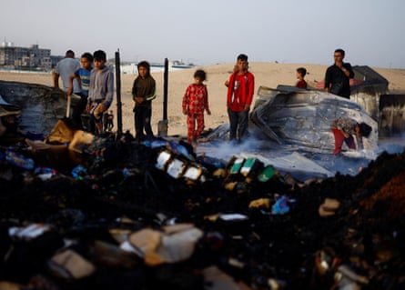 Palestinian children look at the damage to the camp while searching for food among debris at the site of an Israeli strike on an area designated for displaced people in Rafah in the southern Gaza Strip.