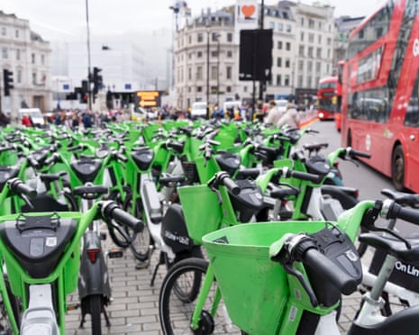 Dozens of Lime bikes parked on pavement as a London red bus drives past