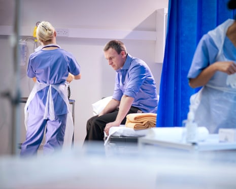 Nurse looking after a man sitting hunched over on a hospital bed
