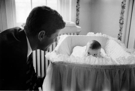 John F Kennedy looks over at his baby daughter Caroline as she lies in her crib in the nursery at their Georgetown home.