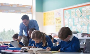 Male teacher assisting elementary school children in classroom during lesson