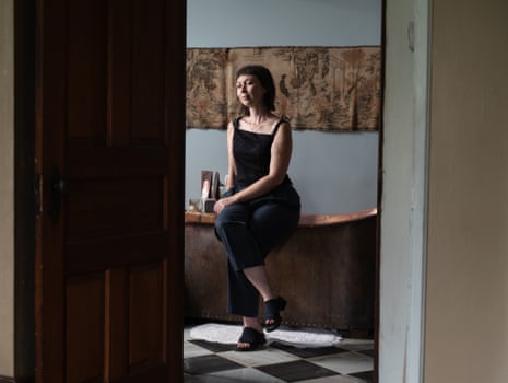 woman sits on the edge of bathtub and looks to side, as seen through doorway