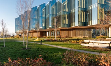 A very modern glass fronted building with angled walls creating a sawtooth effect surrounded by a garden in autumn