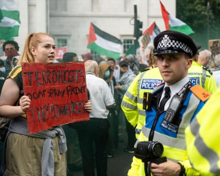 A protester, standing in front of police, holds a placard saying: ‘Terrorists don’t spray paint. They bomb kids.’