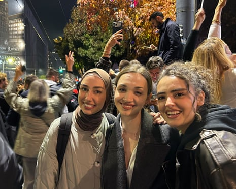 Sara, centre, smiles with two friends amid a crowded nighttime street celebration in Belgrade