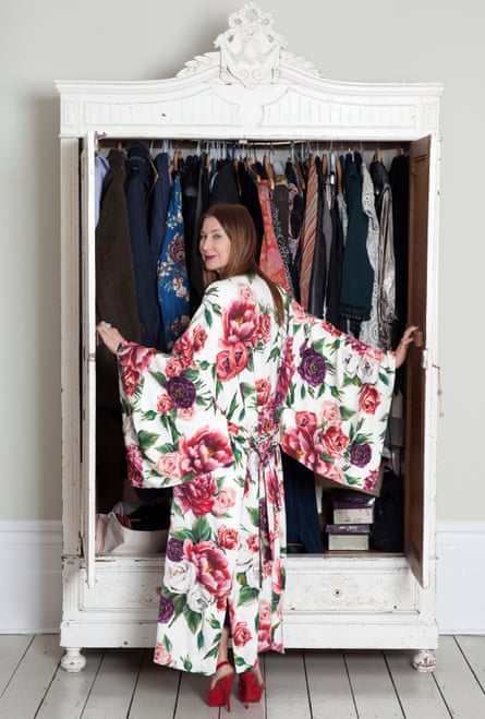 Sharon Walker in a bold floral kimono-type dress and high red shoes opening her wardrobe and looking round at the camera