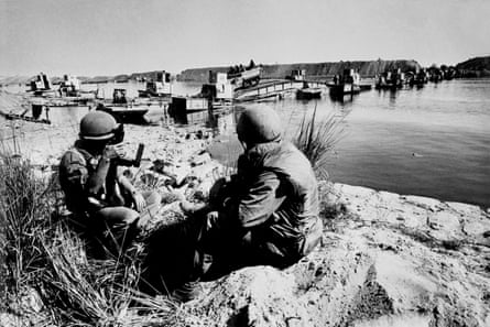solders sit close to the camera, viewed from behind, next to the canal