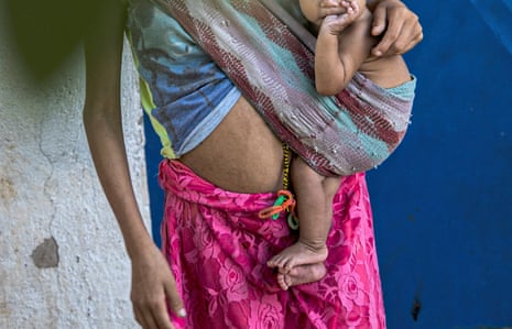 A Indigenous mother holds a baby in a sling on her hip