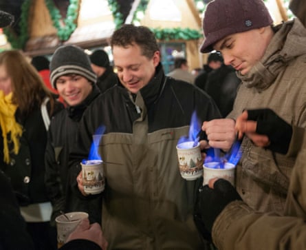 People in winter clothes hold mugs of drinks that have been set on fire