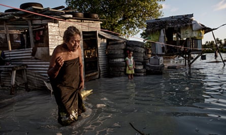 An elderly woman wades through knee-high sea water that has flooded her house in Eita settlement, Tarawa, Kiribati.