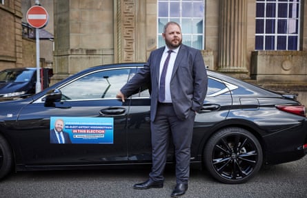 Antony Higginbotham standing in front of a car with a campaign poster on front left door