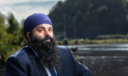 Bearded man in jacket, tie and turban, with river in background.