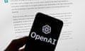 OpenAI logo on a phone in front of a computer screen displaying text