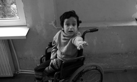 A child sits in a wheelchair, reaching for the photographer