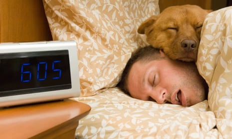 man sleeping deeply with his dog on his face next to alarm clock that says 6 am