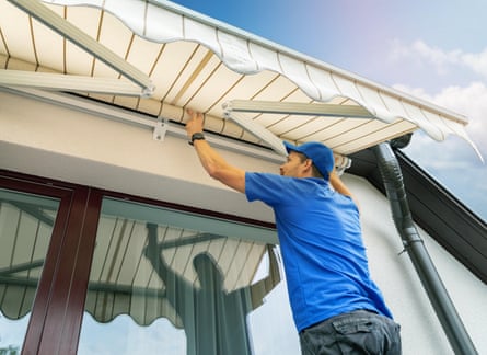 A worker installs an awning on a house wall over a terrace window