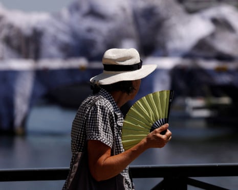 A person wearing a hat and holding a hand fan walks on the Pont des Arts bridge over the River Seine in Paris as temperatures rise during a heatwave affecting a large part of France.
