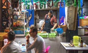 Two customers sit outside the Burmese Restaurant and Library while a chef works at the street food cart, in Chiang Mai, Thailand
