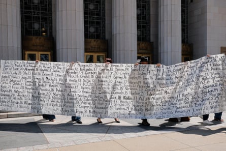 people stand outside courthouse holding long banner with children’s first names and ages