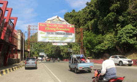 view of road in West Papua, 29 August 2019: small trucks, cars and motorcycles travel beside lush trees and under a large sign
