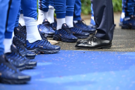 Picture of players feet wearing trainers, facing the shiny black shoes of Macron