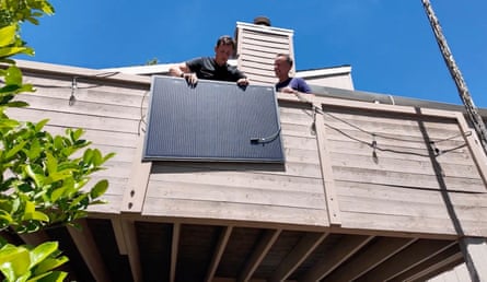 A man holds a solar panel on a balcony as another man looks on