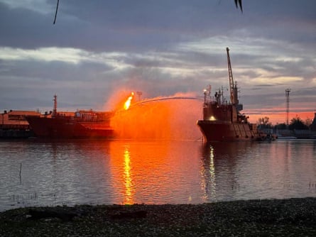 A jet of water directed from a ship at a fire on another ship that has flames leaping 20 metres into the air