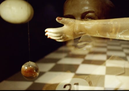 An artificial arm, with red-painted fingernails, throwing a glass apple over a chessboard.