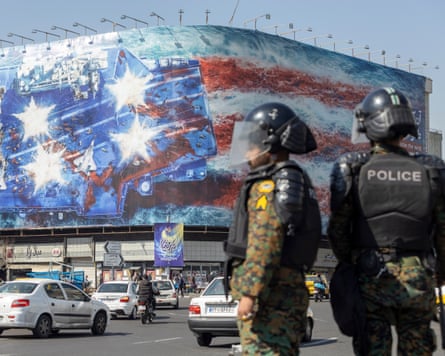 Anti-riot police stand in front of a state building covered with a billboard depicting the destruction of a US aircraft carrier