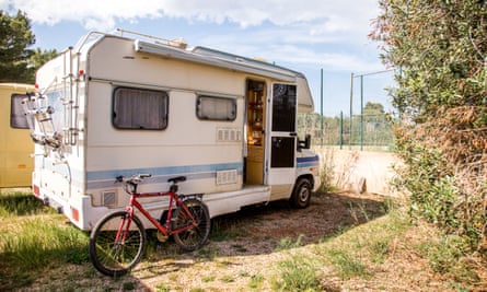 a white camper van is parked in front of a recreation area; a red bicycle is propped against it and a yellow van is parked behind it