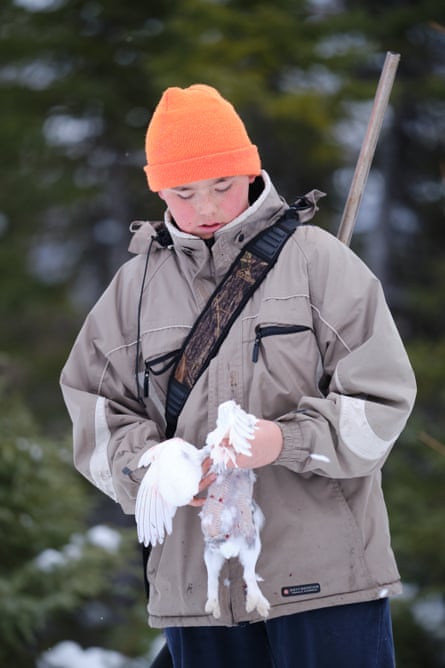 A boy in an anorak with a rifle on his back and a woolly hat holds a white bird