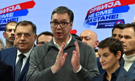 Aleksandar Vucic addresses media at the headquarters of the Serbian Progressive party in Belgrade – he is standing in front of a crowd of party members and speaking behind a microphone; he wears black-rimmed spectacles, a white shirt and grey jumper and is very tall